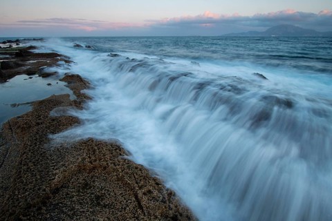 Stunning sunset over the Cadiz coast in Tarifa, highlighting waves cascading over rocky formations.