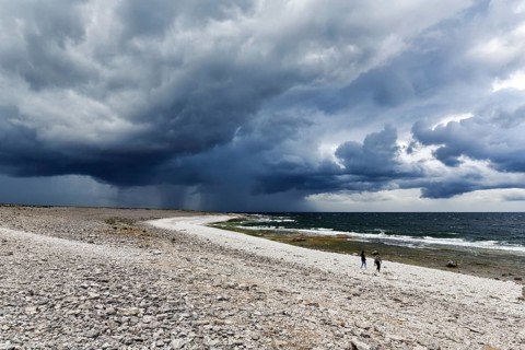 Lonely pebble beach, two hikers, dramatic storm clouds on the horizon, rain showers, Langhammars