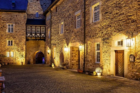Atmospheric evening lighting in a cobbled alleyway between stone walls and old houses, the inner