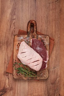Fresh raw duck breasts, on a wooden chopping board, with herbs and spices, no people