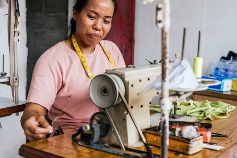 A asian seamstress works diligently at a sewing machine in a tailor shop. Her measuring tape hangs