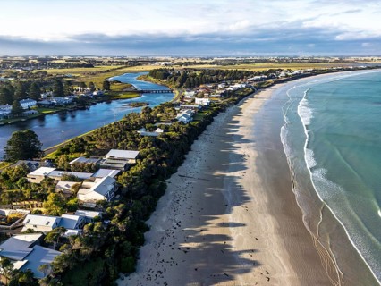 A scenic aerial view showcases a coastal village flanked by a sandy beach and peaceful river,
