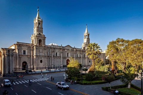 Cathedral on a busy street with cars and park at dusk, The Basilica Cathedral of Arequipa in Peru