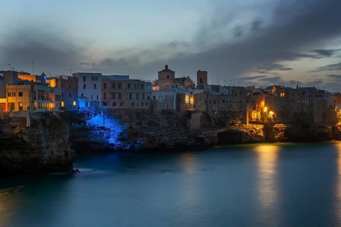 Stunning view of Polignano a Mare's sea cliffs with historic buildings, illuminated by warm lights