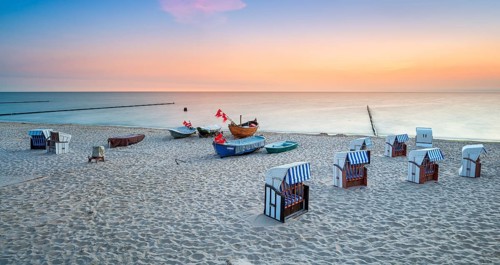 Beach chairs and fishing boats with red flags on fine sandy beach at sunrise, Baltic resort
