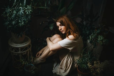 A young woman peacefully sits among lush indoor plants, surrounded by greenery. Her serene