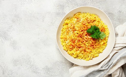 Risotto with shrimp, in a bowl, on a textured surface, with a side dish of fresh coriander,