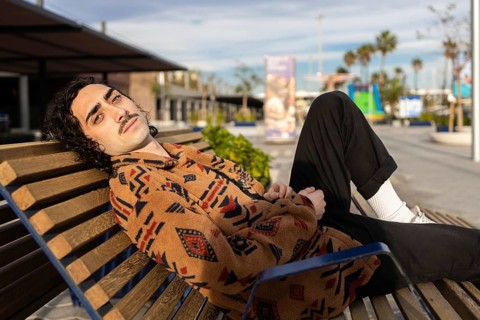 A man in a patterned jacket relaxes on a bench in a sunny urban park Casual and laid-back