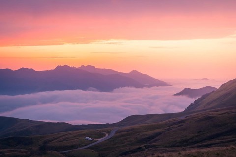 Experience a stunning mountain sunrise as soft pink and orange hues illuminate the sky above