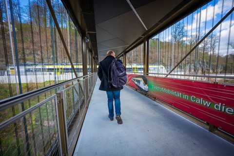 Person walking with backpack across modern bridge next to Zug, Hermann Hesse Bahn, ZOB, Calw,