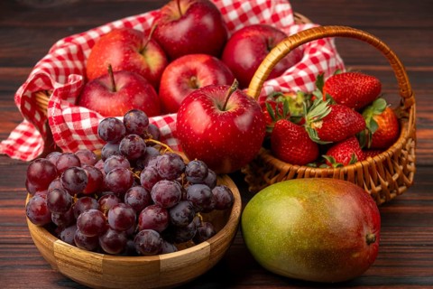 Baskets filled with apples, strawberries, grapes and a mango, arranged on a wooden table