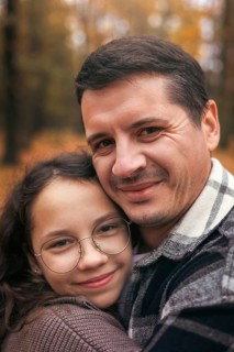 A heartwarming portrait of a father and daughter embracing in a forest during autumn. The warm