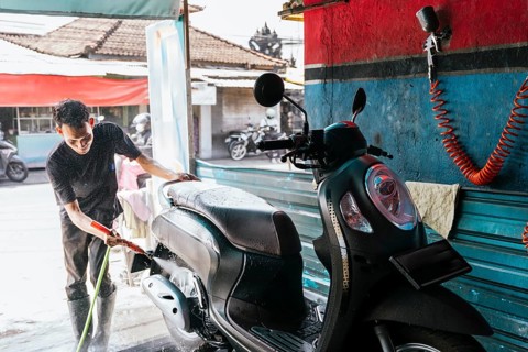 A man cleans a motorcycle using a hose at a car wash. The scene is set in an outdoor environment