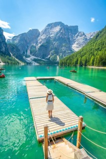 Woman standing on a wooden pier, admiring the stunning turquoise water and majestic mountains of