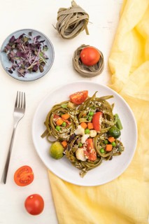 Tagliatelle green spinach pasta with tomato, pea and microgreen sprouts on a white wooden
