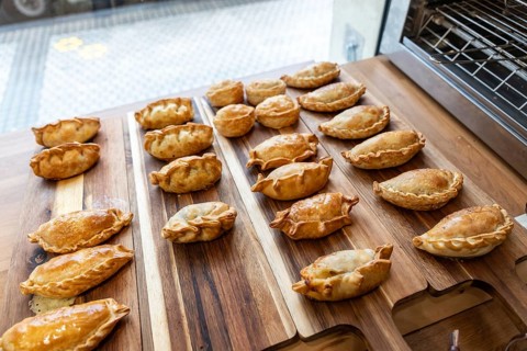 Golden brown empanadas and small round pastries arranged on a natural wood serving board, ready for