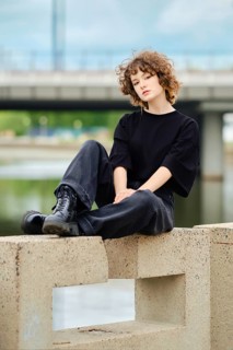 Portrait of smiling teenager girl in black jeans, t-shirt and rough boots near the river