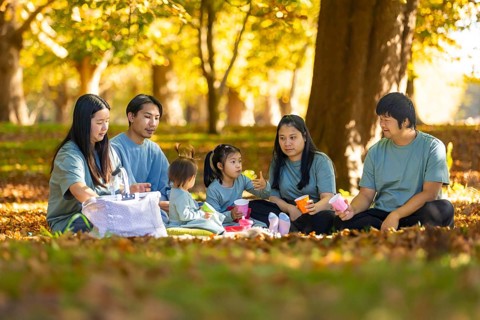 An Asian family gathers for a heartwarming picnic in a sunlit park during autumn. Surrounded by