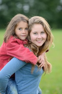 Girl carries her little sister piggyback outdoors, Germany