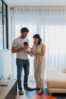 A father and mother stand together in a warm, light-filled living room, lovingly holding their