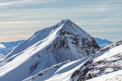 A stunning view of a snow-covered mountain peak basking in sunlight under a clear blue sky. The