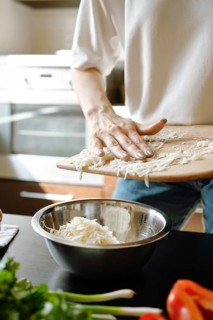 Unrecognizable woman pouring grated cheese into a bowl in the kitchen