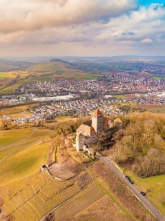 A fascinating castle overlooks extensive fields and a village, nestled in a hilly landscape,