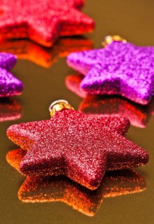 A close-up image featuring a collection of glittering Christmas stars in red and purple shades