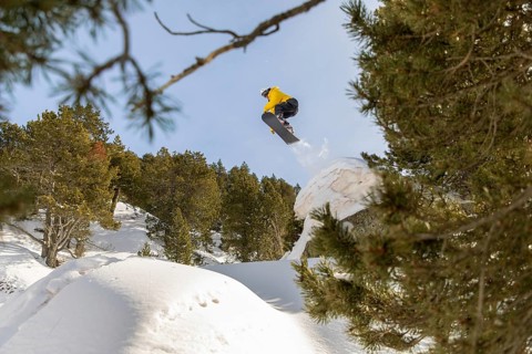 A snowboarder dressed in vibrant gear executes an impressive jump off a snowy ridge in the