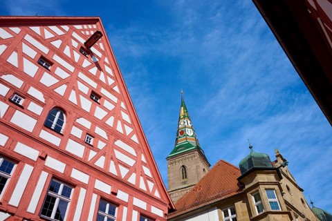 Close-up of a half-timbered house with a view of an ornate church tower in the background,