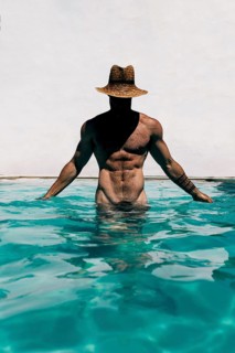 Unrecognizable fit man wearing a hat, standing in a swimming pool naked, with toned muscles