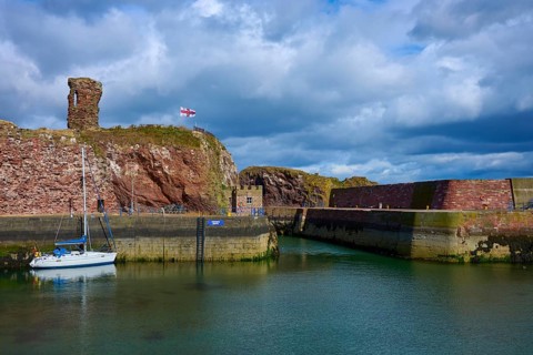 A harbour with a sailboat, an old tower and calm water under cloudy sky, Dunbar, East Lothian,