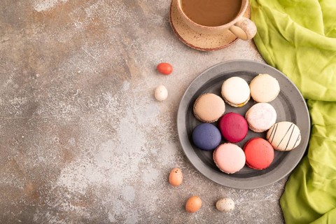 Macarons colourful cookies dessert, cup of coffee, on brown concrete background with green linen