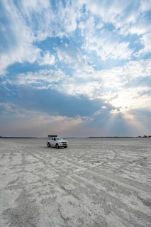 Toyota Hilux off-road vehicle on a salt pan, dramatic clouds with sunbeams, wide open plain, Nxai