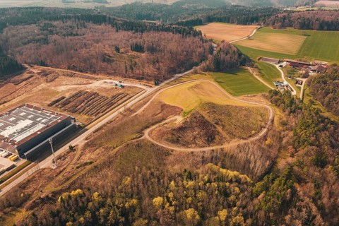 Industrial building surrounded by fields and forests, hills in the background, from a bird's eye