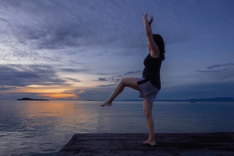 A tourist practices yoga at sunset on a wooden pier, surrounded by the serene waters of Waigeo