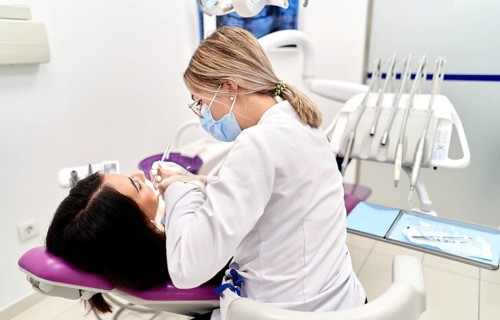 A dentist in a face mask conducts a dental check-up in a modern clinic. The patient is seated in a