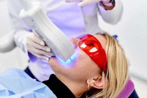 A patient undergoes a professional teeth whitening treatment at a dental clinic, wearing protective