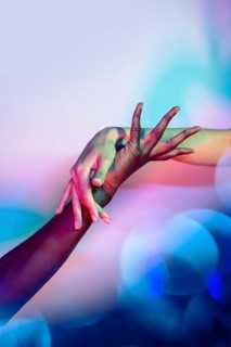Multiethnic hands interlocked in a creative display under vibrant, colorful lighting. This artistic