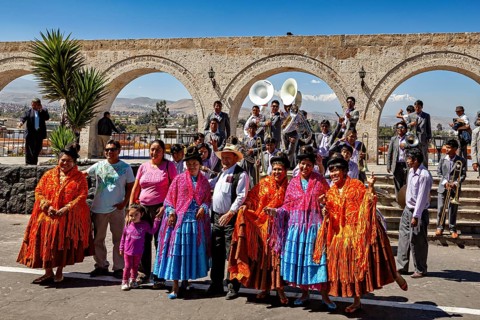 A group of people in traditional colorful clothes with a wind band and bows in the background, a