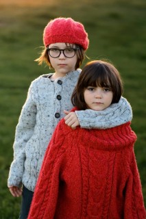 Two siblings, a young girl and a boy, wrapped in cozy sweaters, enjoy the warmth of a golden autumn