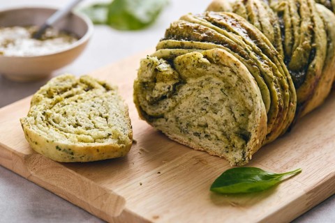 Baked homemade savoury babka plaited bread loaf flavoured with pesto on wooden bread board