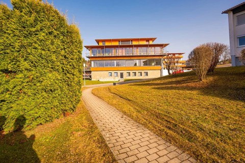 Well-maintained path leads to a modern building flanked by a hedge under a sunny sky, Hochgrat