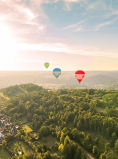 Hot air balloons flying over wooded hills in a landscape at sunset, Calw, Black Forest, Germany