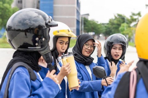 A group of Asian Muslim students wearing helmets and school uniforms gather on campus, preparing