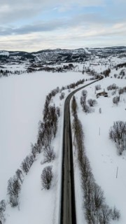 A stunning aerial view captures a road cutting through a serene snow-covered Nordic landscape. The
