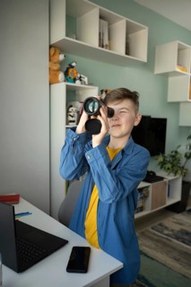 Young boy enthusiastically looks through a monocular in a modern living room, displaying a sense of