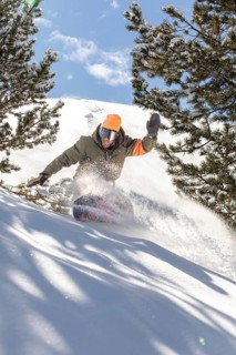 A snowboarder expertly navigates through fresh powder in the backcountry, surrounded by