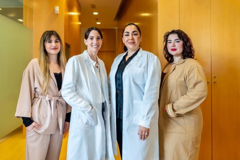 Four smiling women, two wearing white lab coats and two in professional attire, standing together