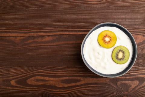 Yogurt, with kiwi in blue bowl on brown wooden background, top view, flat lay, copy space,